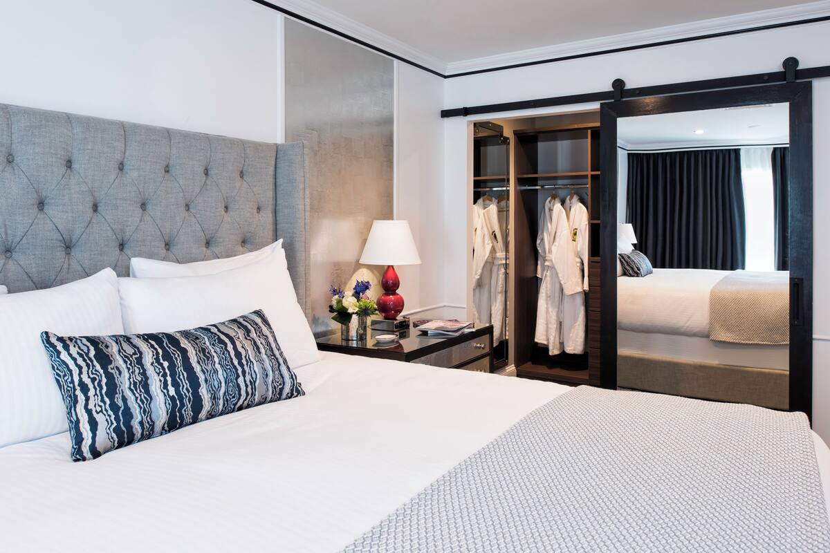 A hotel room with a large bed, a bedside table with a lamp, a mirror, and a walk-in closet.