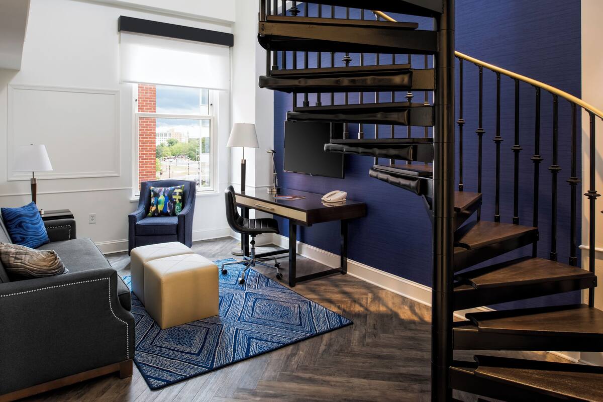 A modern living room with a dark staircase, a desk, and a view of the outdoors.