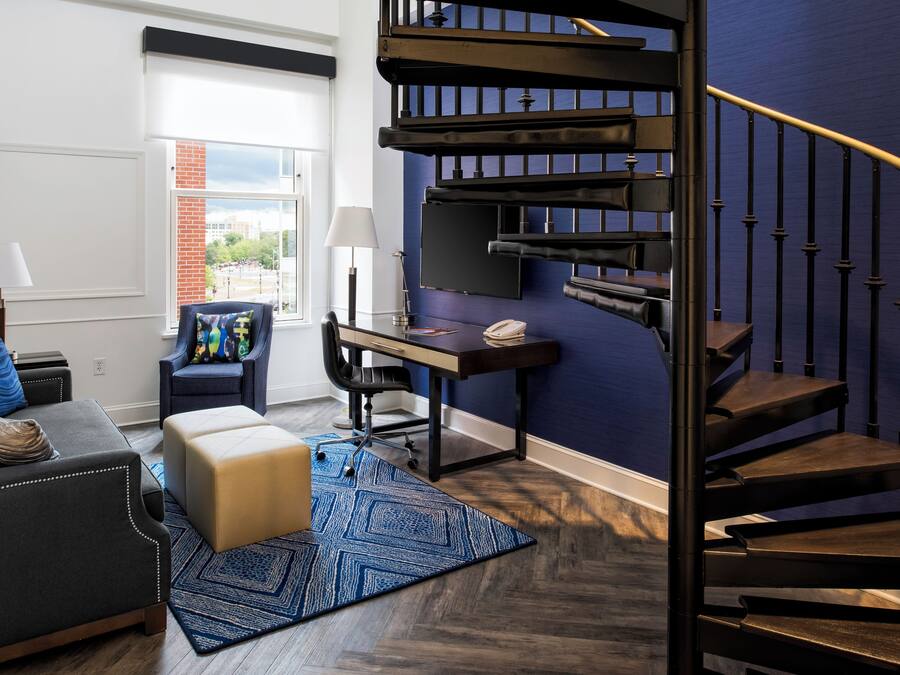 A modern living room with a dark staircase, a desk, and a view of the outdoors.
