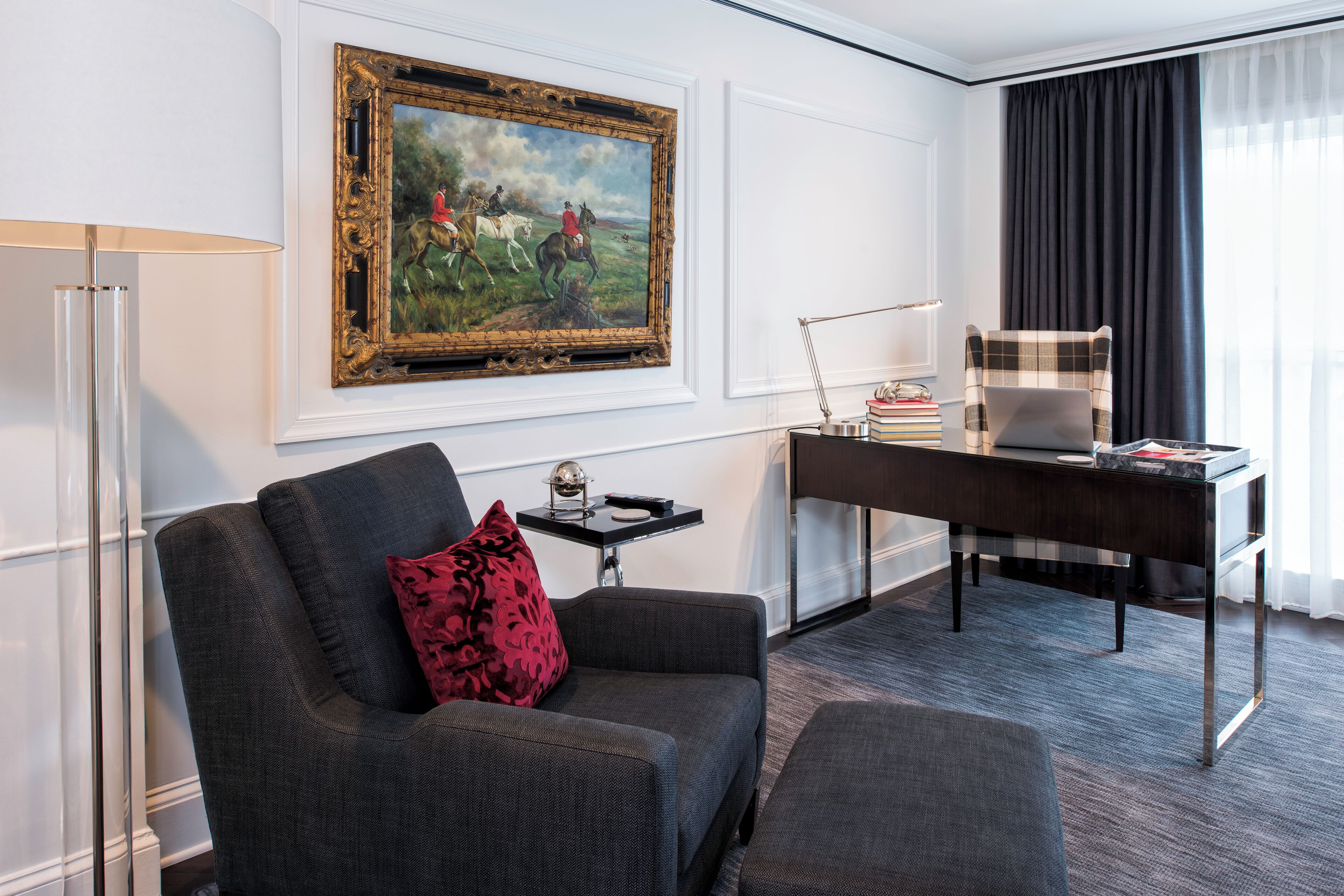 Une chambre moderne avec un canapé, un bureau, une lampe, une chaise et un tableau encadré au mur.
