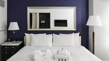 A neatly made bed with white linens, a large mirror above it, and a bedside table with a lamp and a clock.