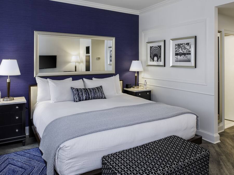 A bedroom with a large bed, two bedside tables, a mirror, and framed pictures on the wall.