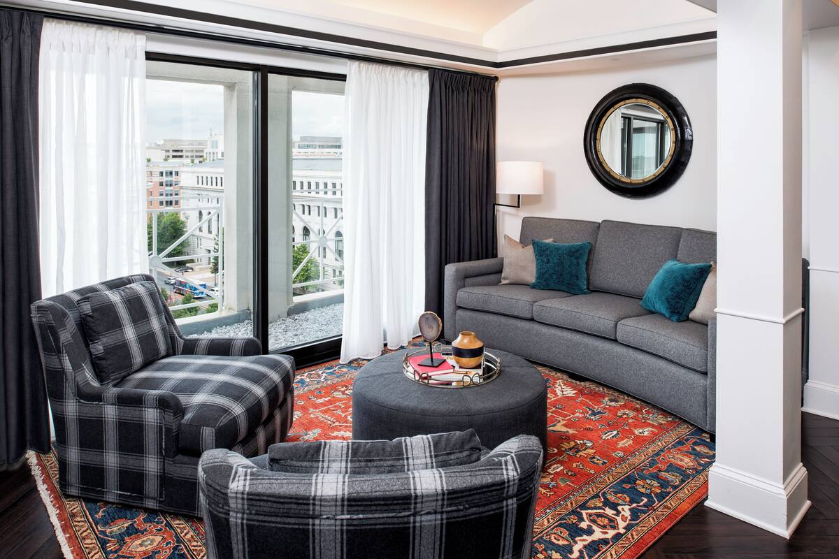 A modern living room with a sofa, armchair, ottoman, and a large window with curtains.