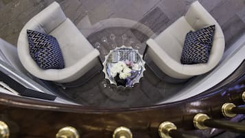 A top-down view of a modern interior with two white armchairs with patterned cushions, a glass table with a floral arrangement, and a dark wooden structure with brass details.
