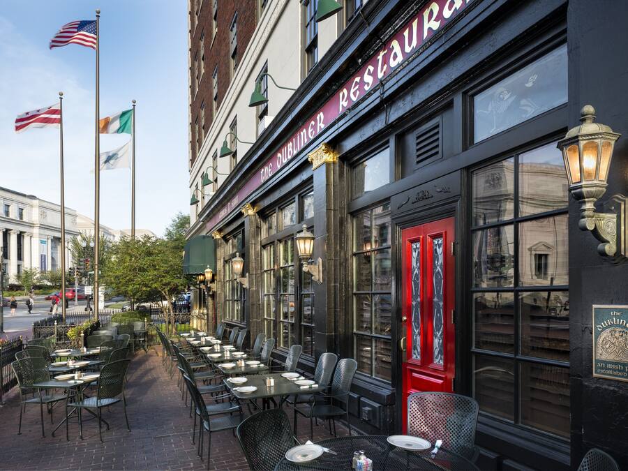 An outdoor seating area with tables and chairs, a red door, and flags on poles.