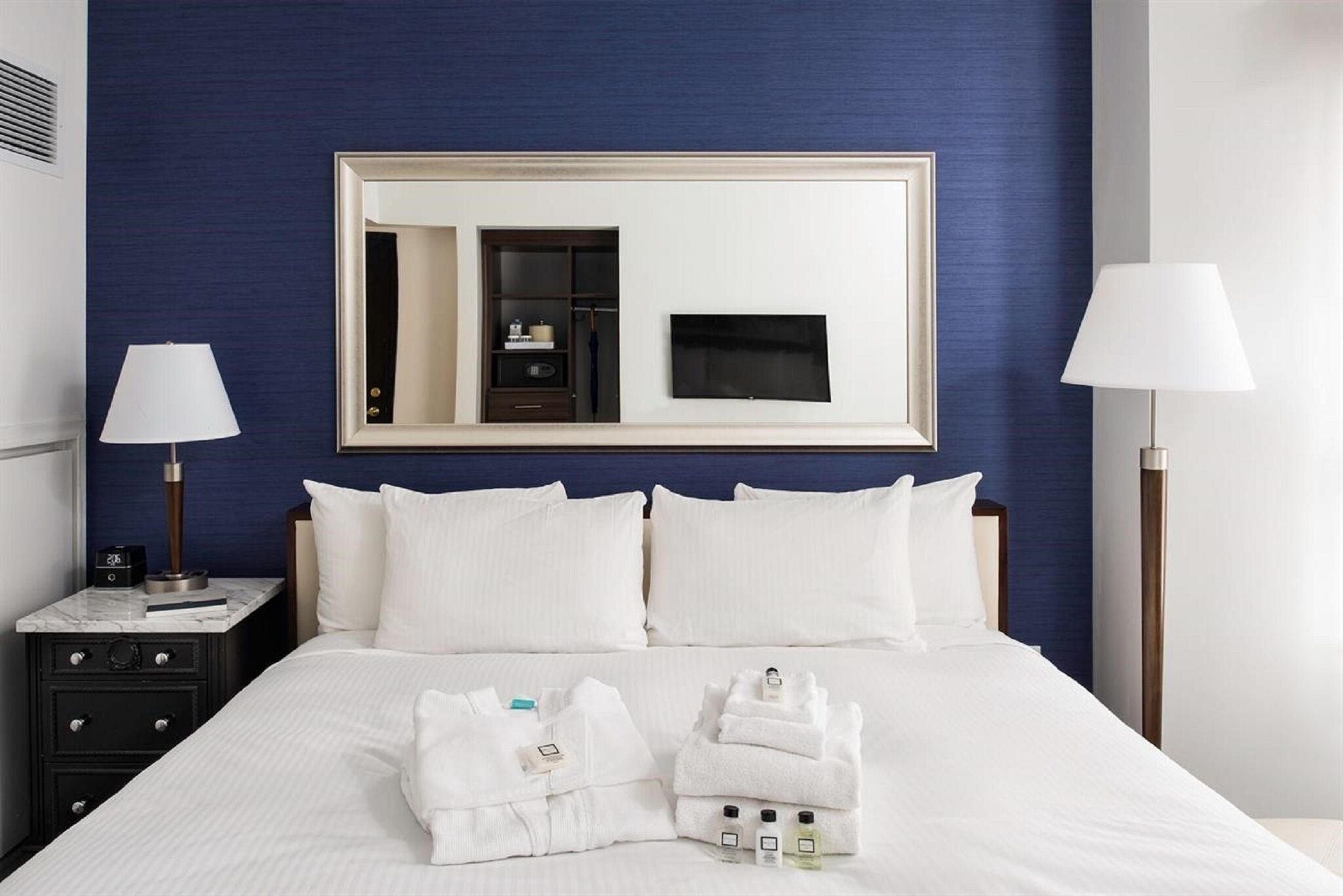 A hotel room with a large bed, two bedside tables, a mirror, and a TV.