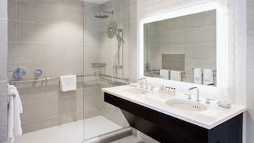 A modern bathroom with a glass shower enclosure, dual sinks, and a large mirror.
