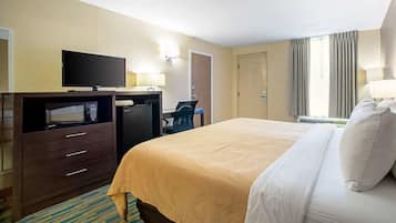 A hotel room with a bed, a desk with a computer, a television, and a microwave.