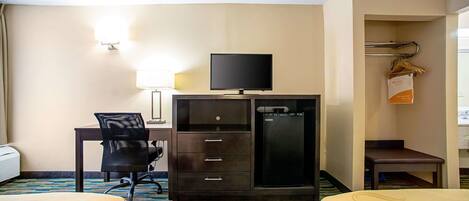 A hotel room with two beds, a desk with a chair, a television, a minibar, and a coat rack.