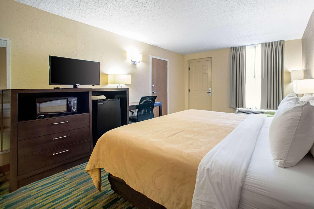 A hotel room with a bed, a desk with a computer, a television, a microwave, and a door.