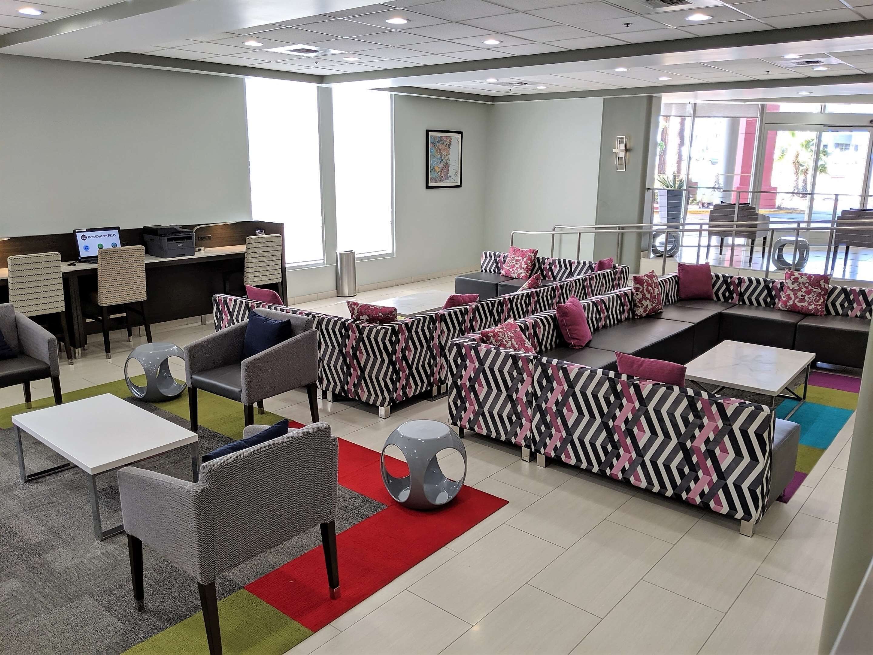 A modern lounge area with seating arrangements, a reception desk, and a large window providing natural light.