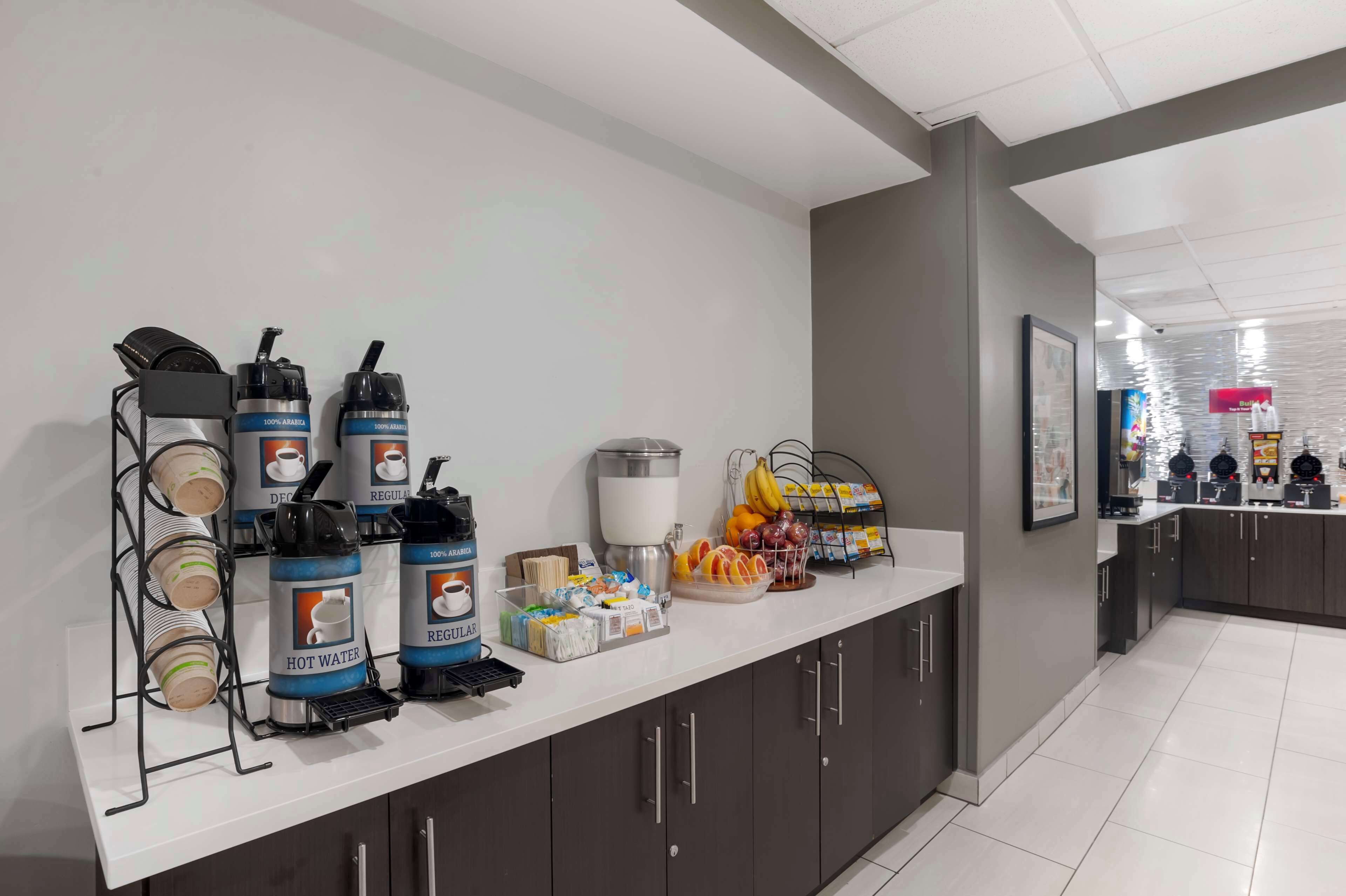 A breakfast bar with hot water dispensers, coffee machines, and a fruit display.