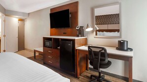 A hotel room with a bed, a desk with a chair, a TV, a refrigerator, a lamp, and a coffee maker. - Best Western Plus Commerce Hotel (Los Angeles)