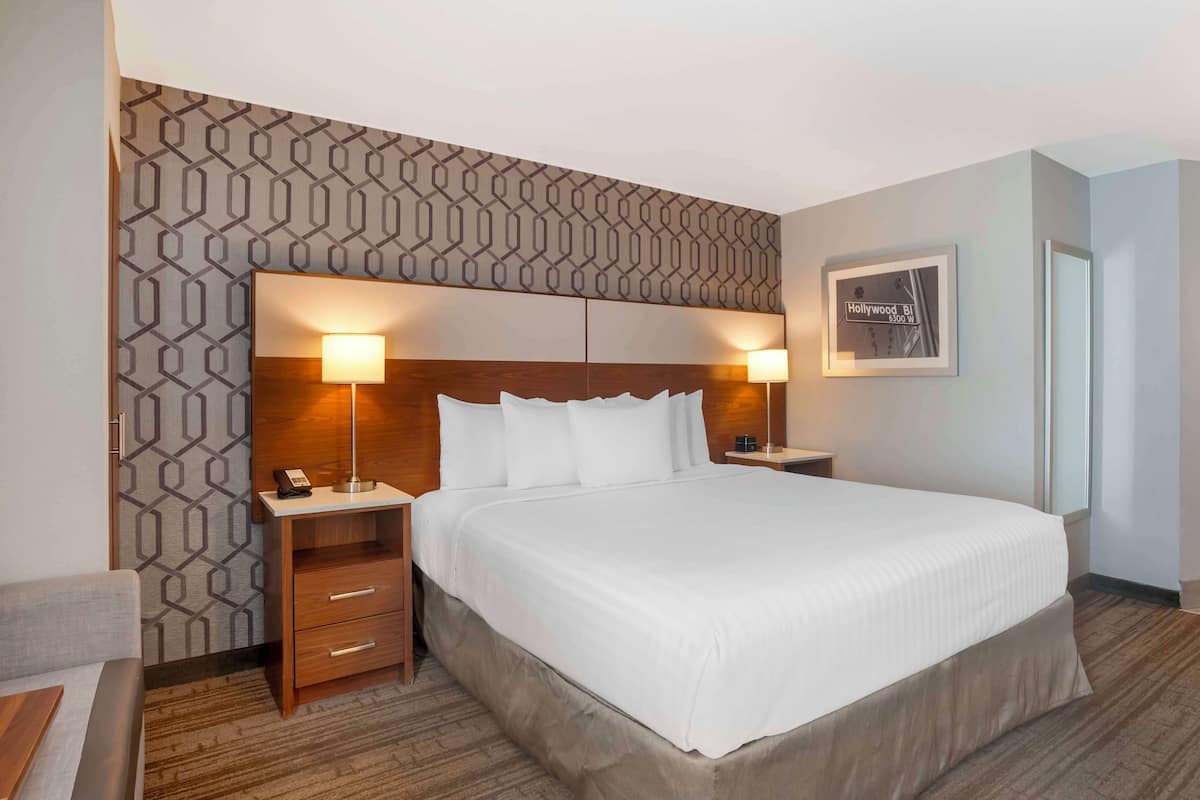 A hotel room with a large bed, two bedside tables with lamps, a patterned wall, and a framed picture on the wall.