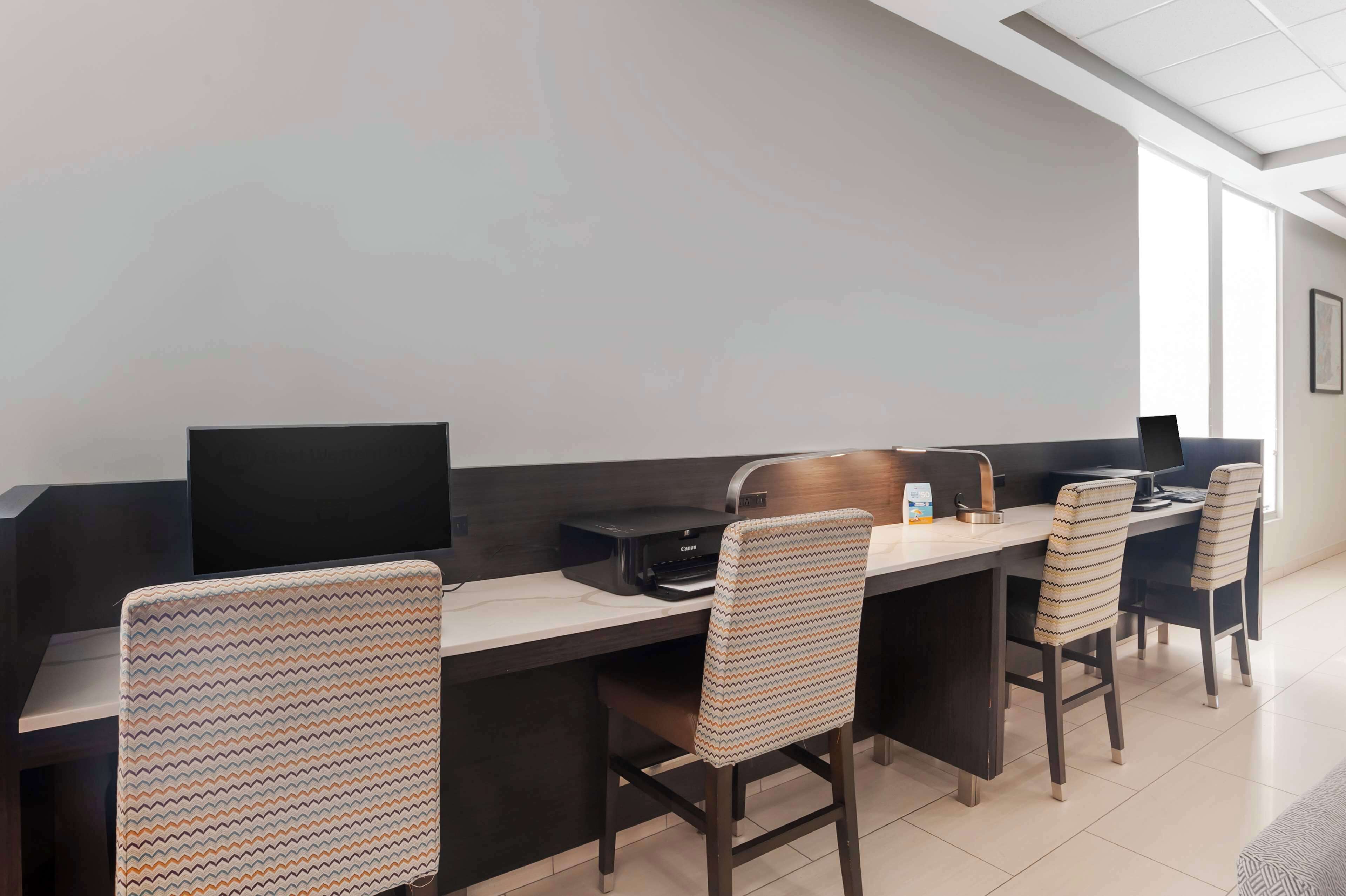 A modern office space with a long desk, multiple chairs, and a flat-screen monitor.
