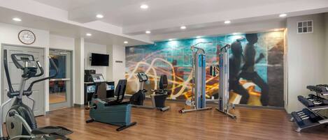 Uma academia com equipamentos de cardio, aparelhos de musculação e um grande espelho.