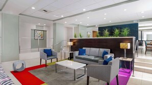 A modern lobby with a grey sofa, armchairs, a white coffee table, and a colorful rug. - Best Western Plus Commerce Hotel (Los Angeles)