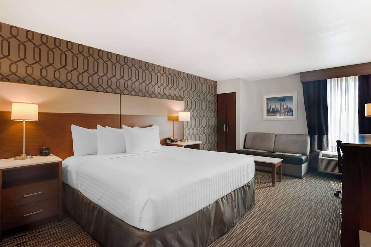 A hotel room with a large bed, bedside lamps, a desk, a chair, and a sofa.