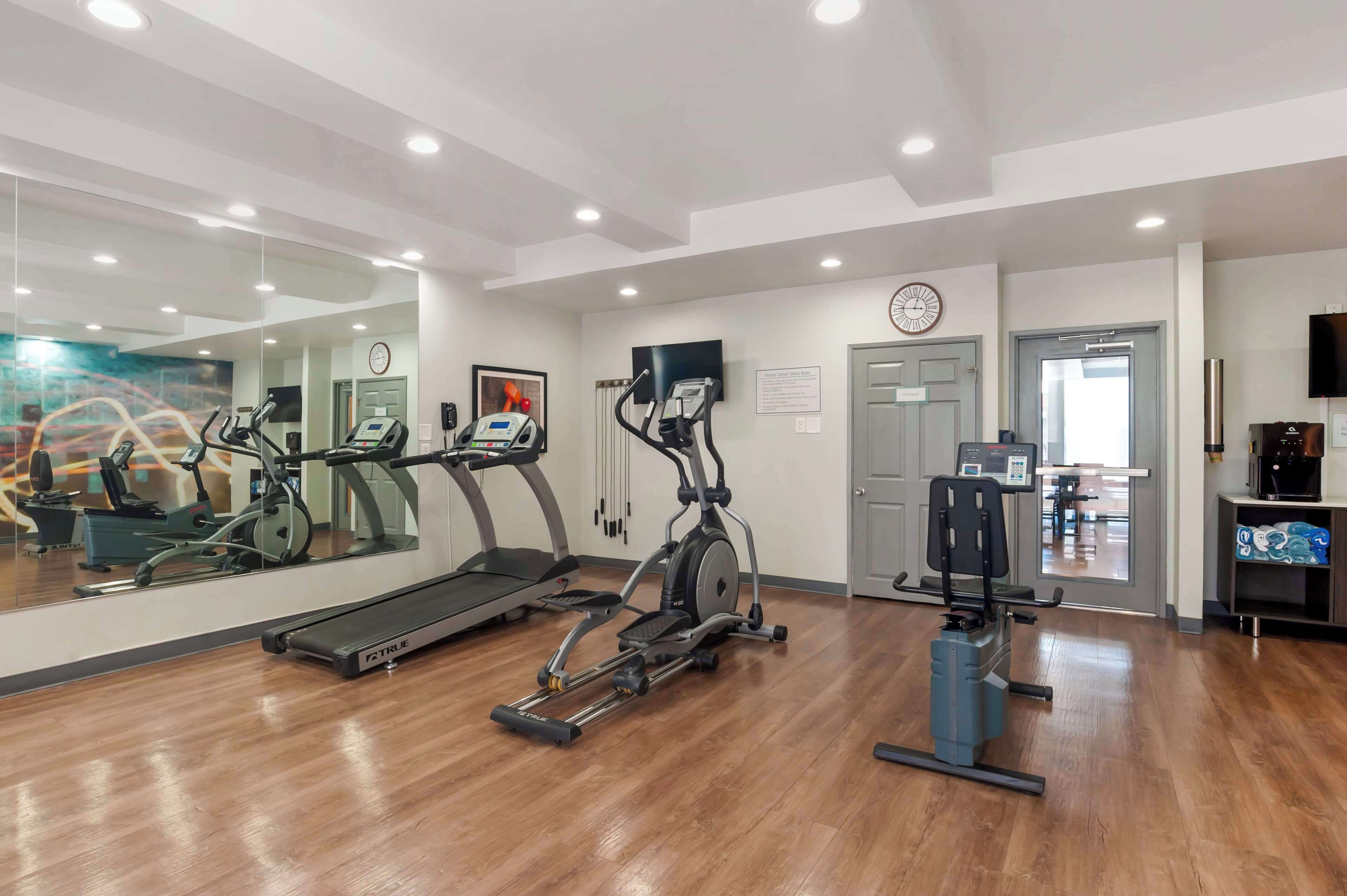 A gym with cardio machines, a mirror, a clock, and a television.