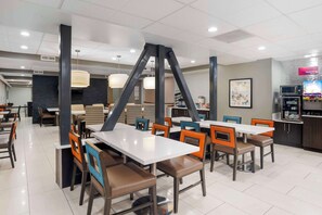A modern dining area with white tables and chairs, black structural columns, and a kitchen area with appliances and a refrigerator. - Best Western Plus Commerce Hotel (Los Angeles)