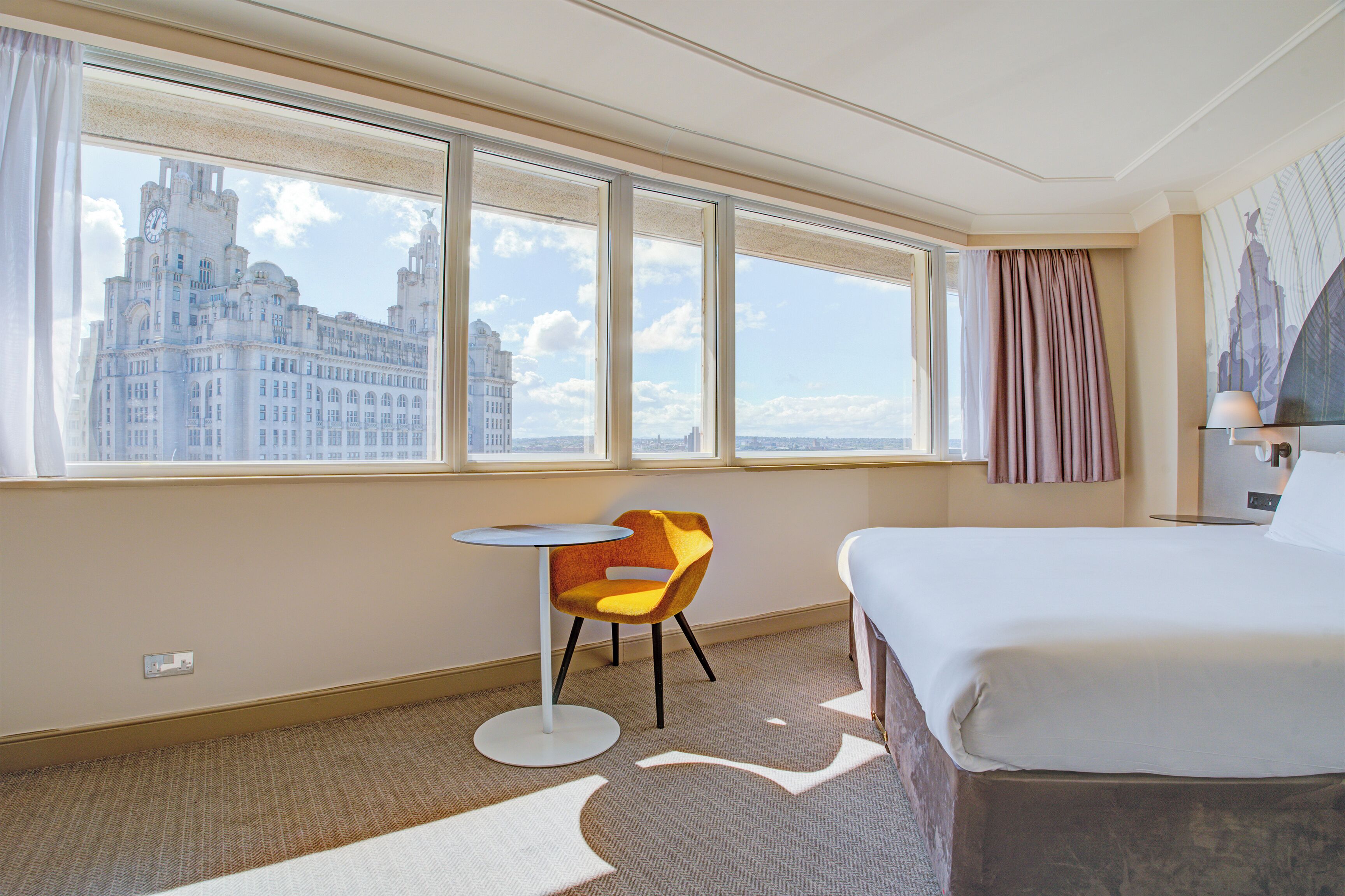A hotel room with a large window, a bed, a round table, and a chair.