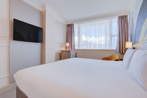 Una habitación de hotel con una cama grande, un televisor de pantalla plana montado en la pared, un escritorio con lámpara y una silla.