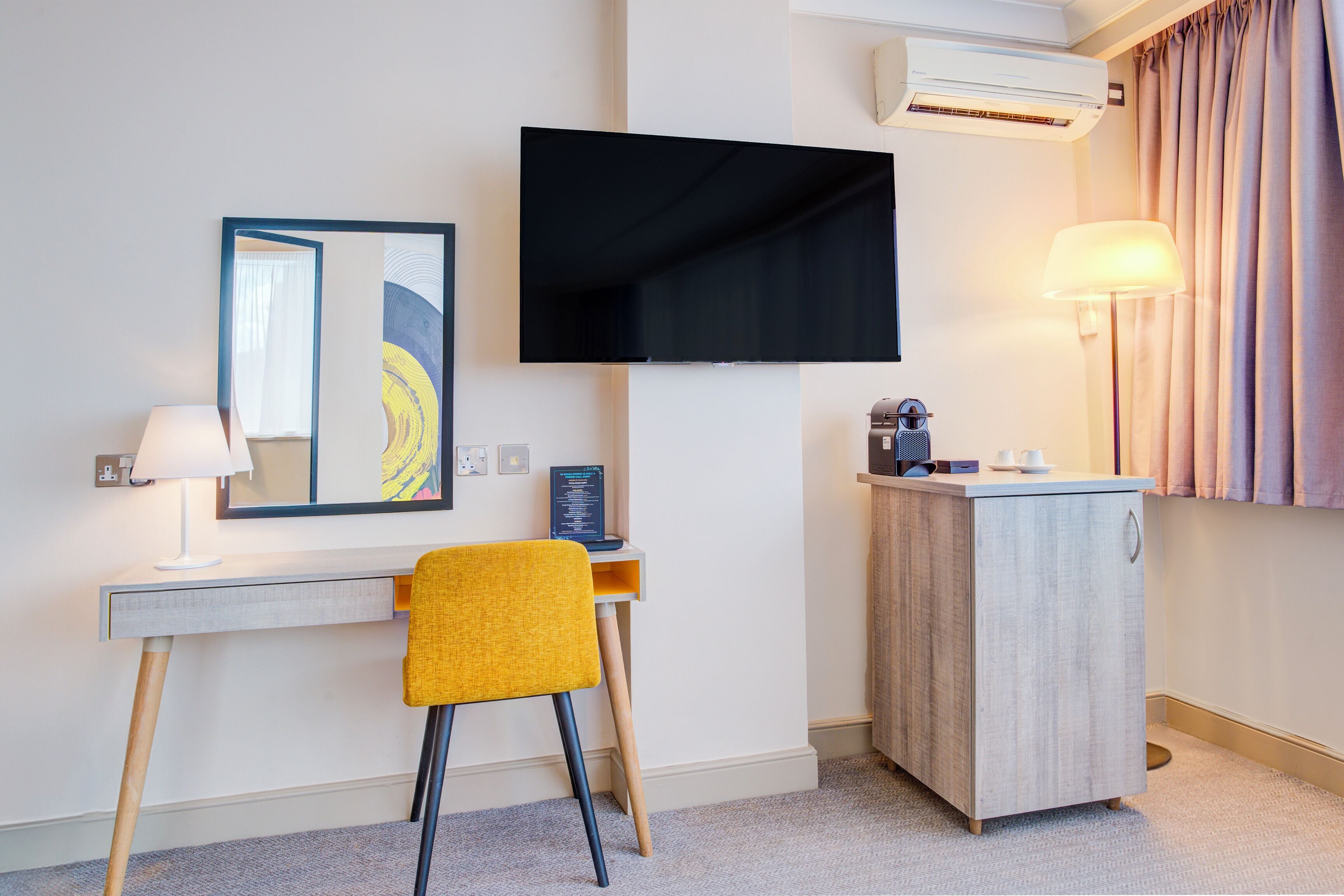 Habitación de hotel con escritorio, silla, televisor y minibar.