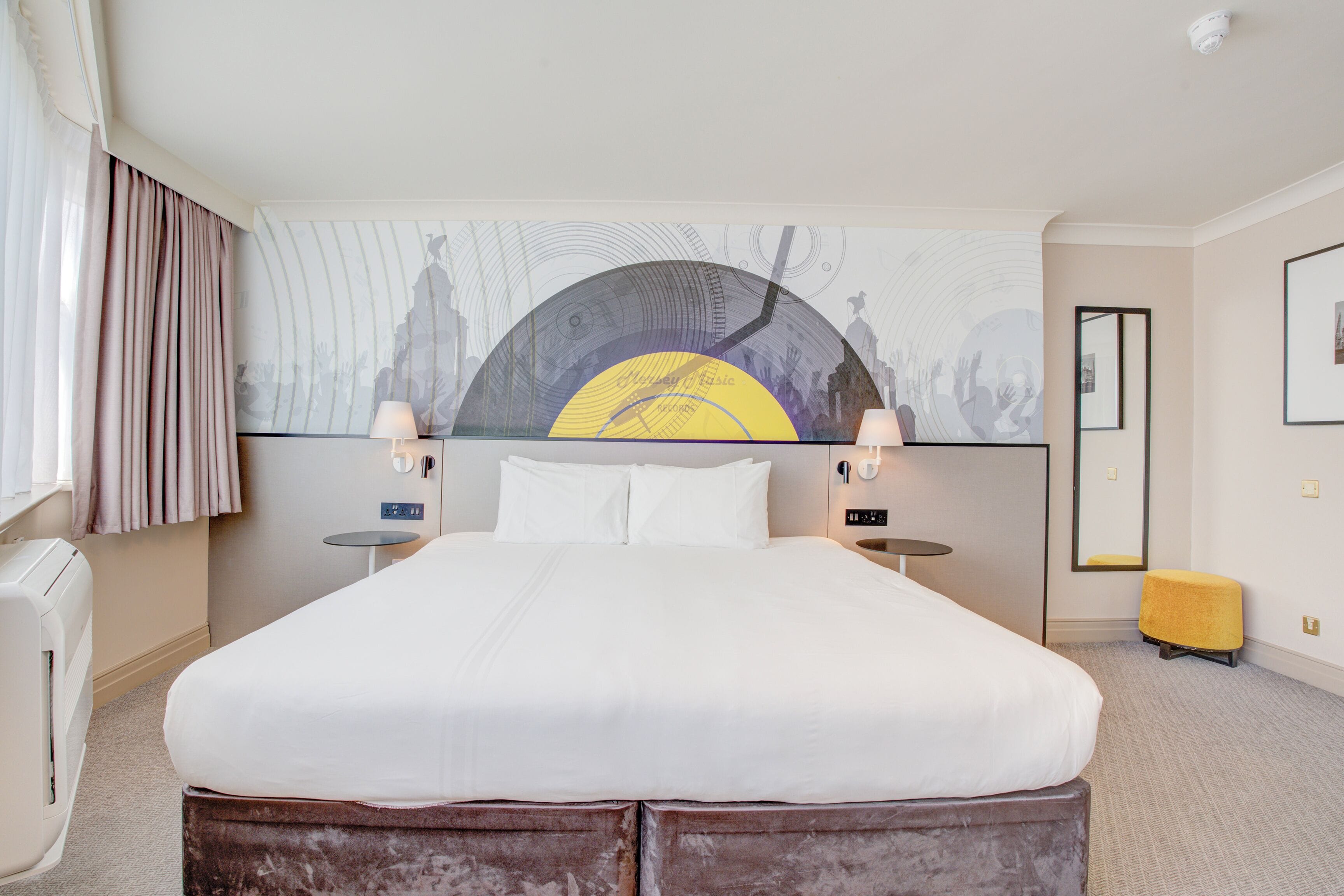 Ein Hotelzimmer mit einem großen Bett, zwei Nachttischen, einem Spiegel und einem Wandbild.