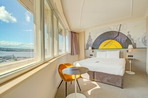 A hotel room with a large window, a bed, a round table, and a chair.