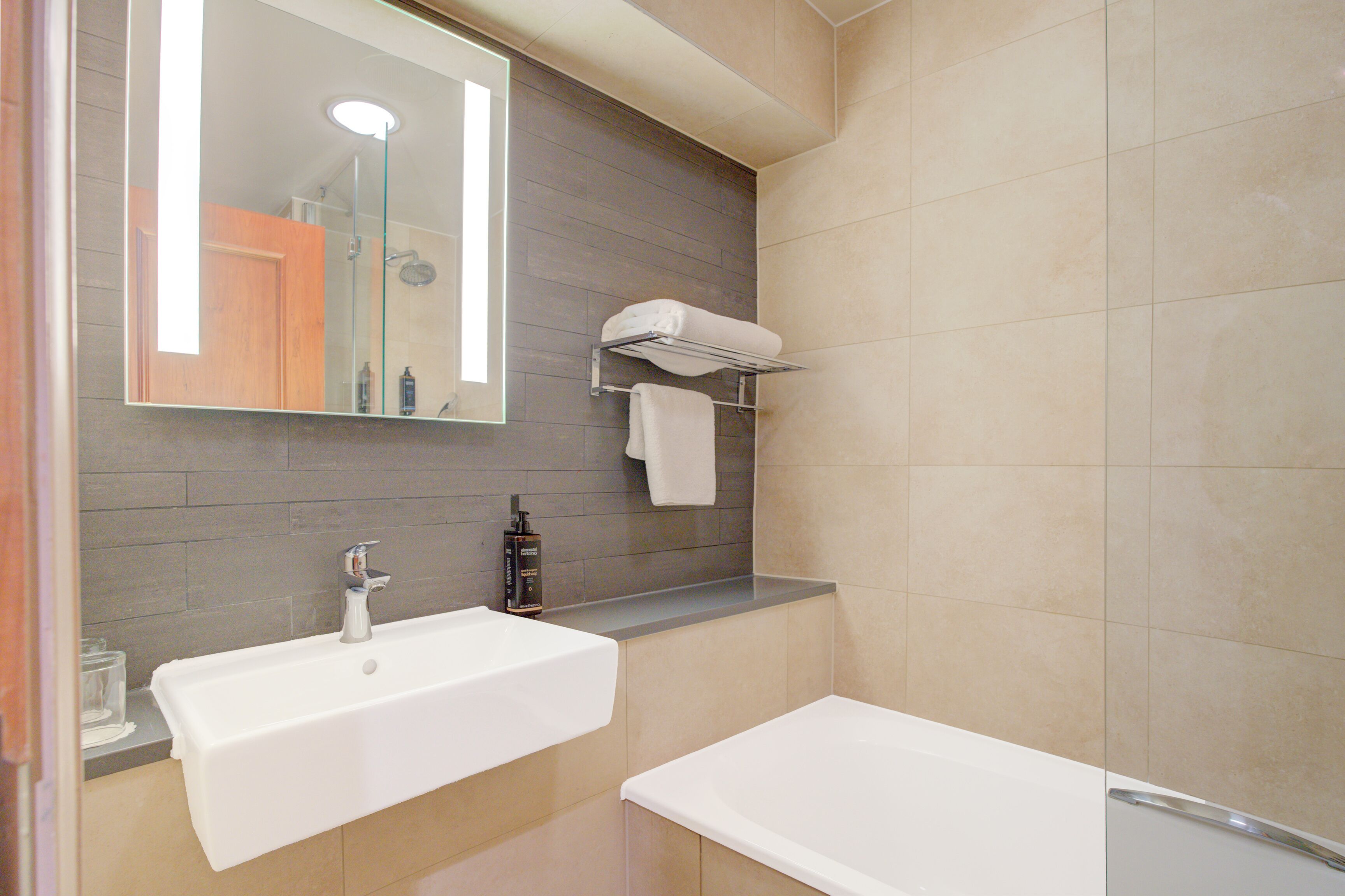 A modern bathroom with a large mirror, two sinks, a shower, and a towel rack.