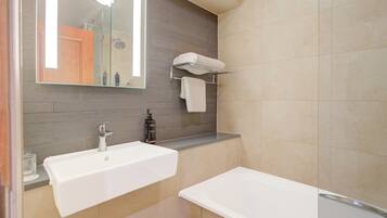 A modern bathroom with a large mirror, two sinks, a shower, and a towel rack.