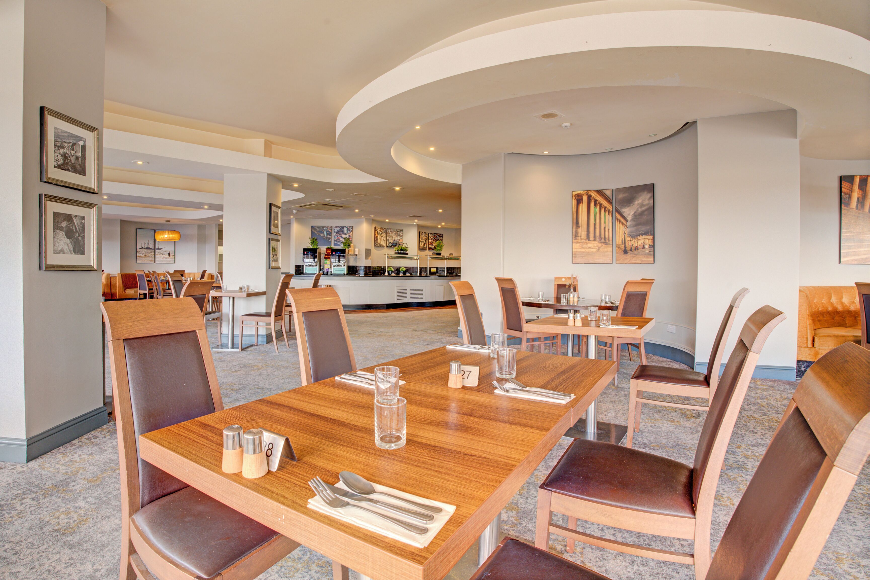 A dining area with wooden tables and chairs, a bar in the background, and framed artwork on the walls.
