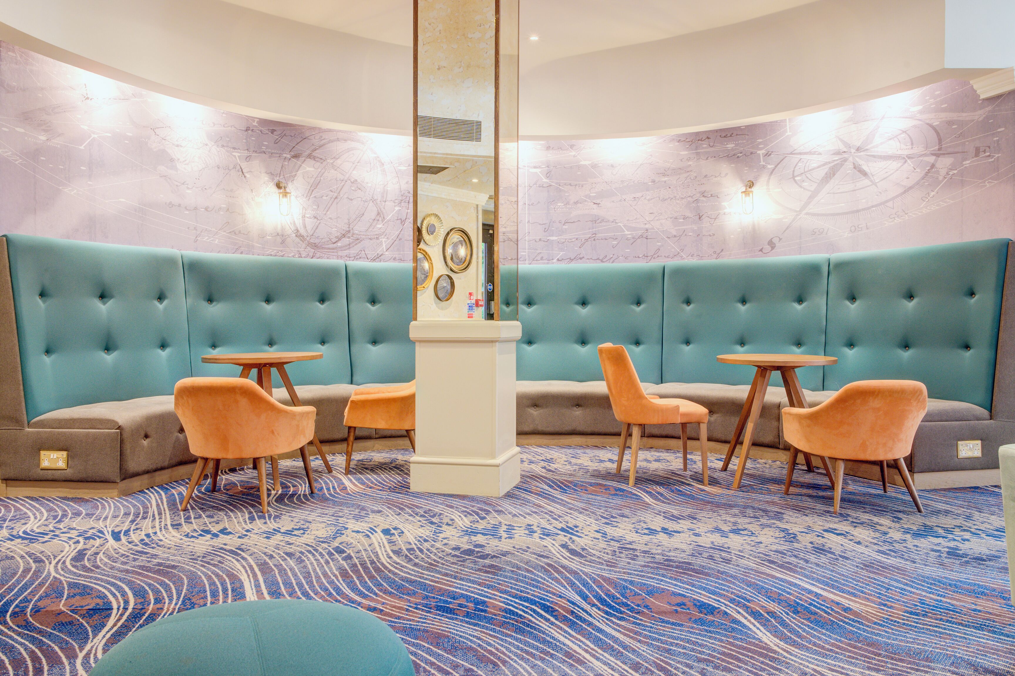 A modern lounge area with teal upholstered sofas, wooden tables, and orange chairs.