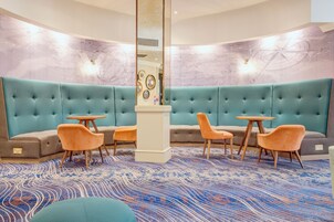 A modern lounge area with teal upholstered sofas, wooden tables, and orange chairs.