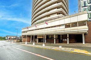 Un hotel de varios pisos con fachada plana, varios balcones y una entrada al estacionamiento.
