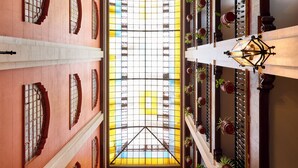 A corridor with a central stained glass window, flanked by walls with arched windows and potted plants. - Best Western Majestic (Mexico City)