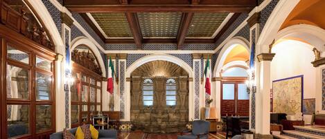 A grand lobby with a high ceiling, ornate wooden furniture, and a stone fireplace.