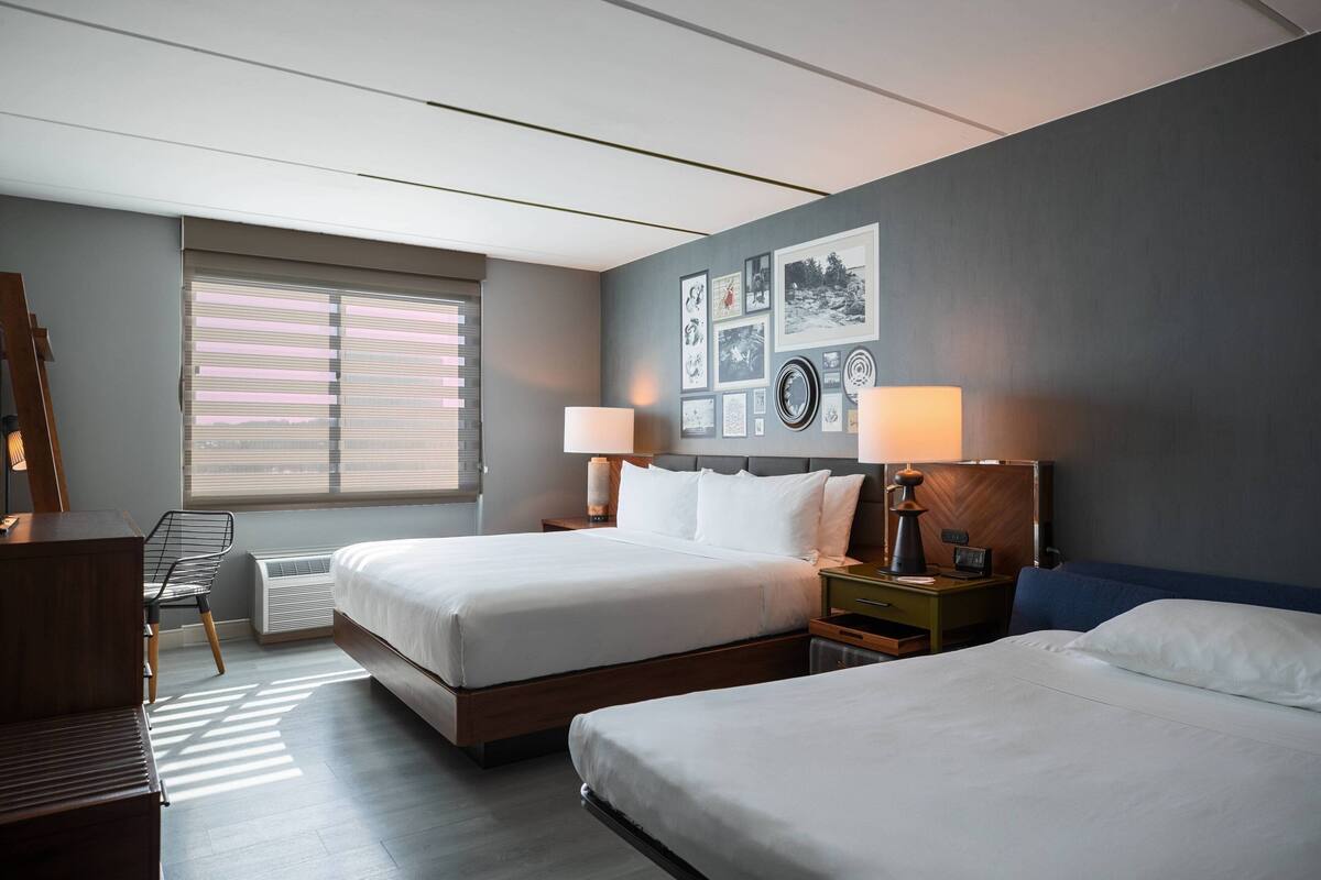 A hotel room with two beds, a desk, a chair, and a wall with framed pictures.