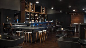 A bar area with wooden shelves stocked with bottles, a bar counter, and stools. - Renaissance Minneapolis Bloomington Hotel (Bloomington)