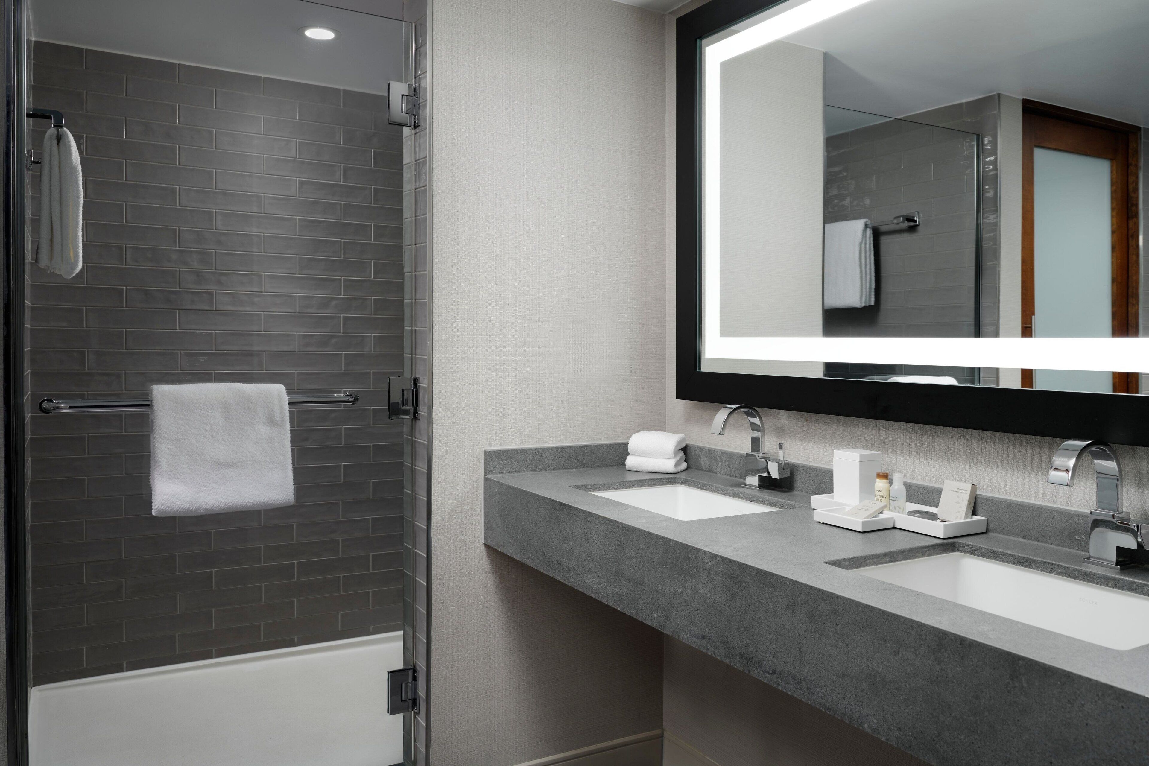 Un baño moderno con cabina de ducha de vidrio, dos lavamanos, un espejo grande y un perchero para toallas.