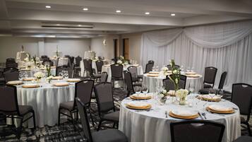 Un salón de banquetes con mesas redondas dispuestas para el servicio de comidas, cada una con manteles blancos, platos de carga dorados y centros de mesa florales.