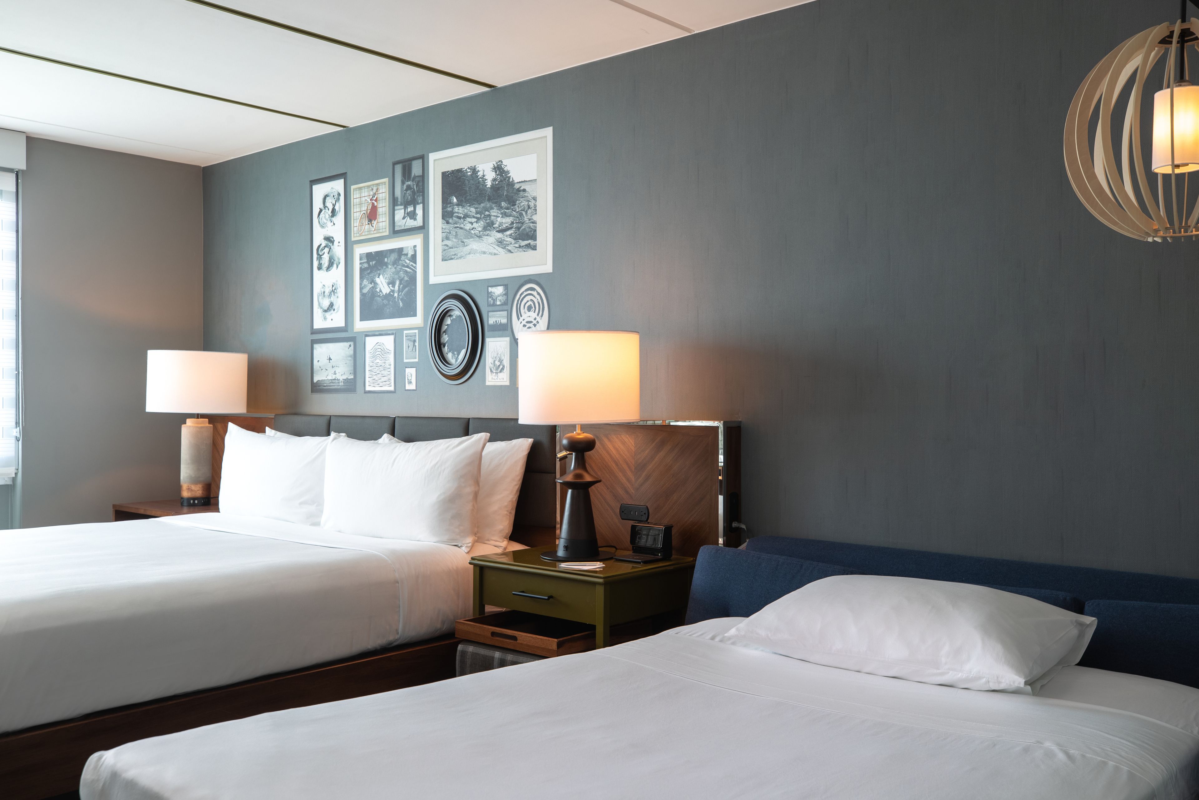 A hotel room with two beds, a nightstand with a lamp, and a wall decorated with framed pictures.