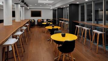A modern dining area with high wooden tables and chairs, large windows, and a clean, minimalist design.