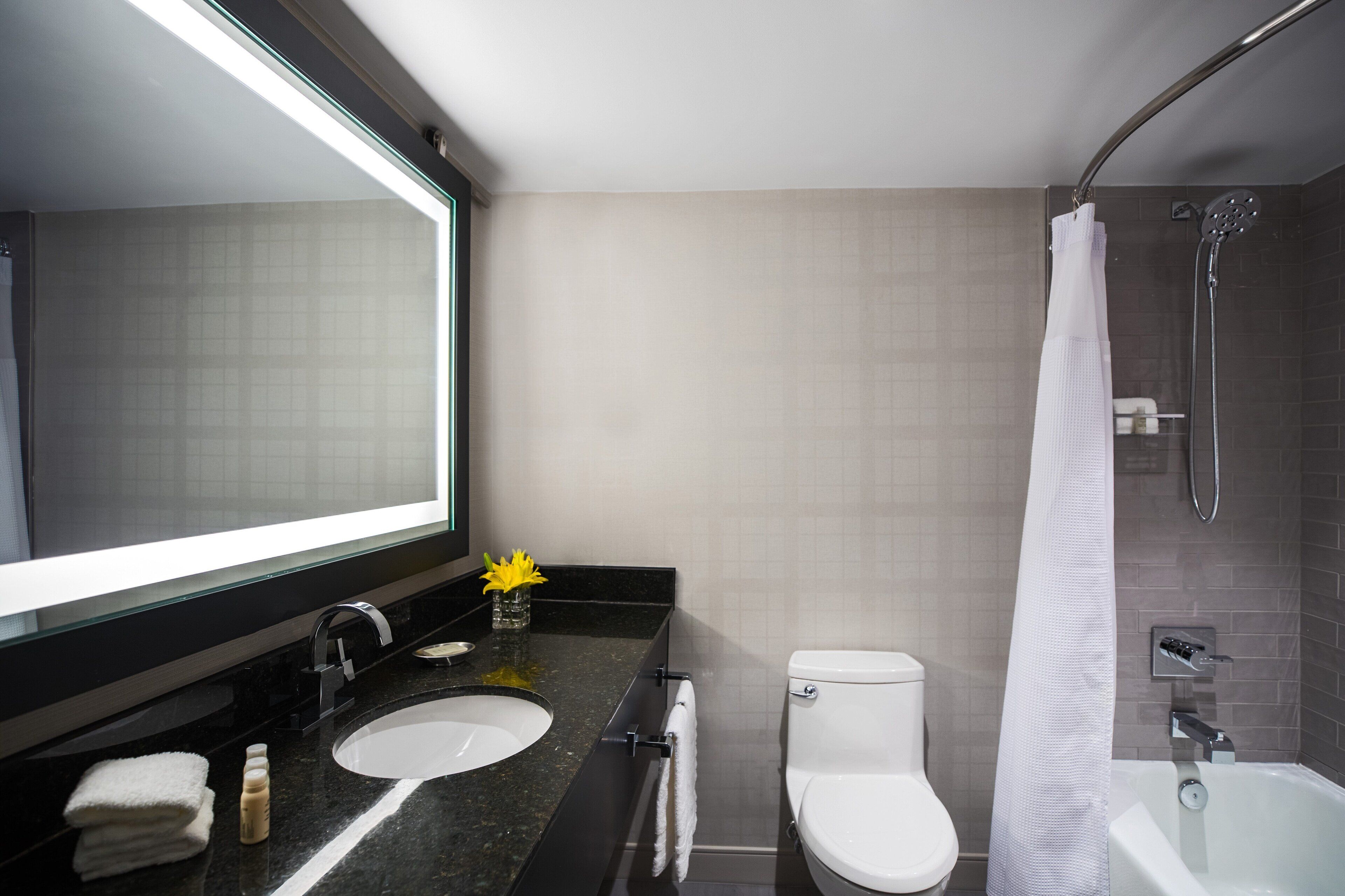 Un baño moderno con un espejo grande, un lavamanos, un inodoro y una bañera.