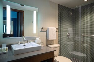 Un baño moderno con un espejo grande, un lavamanos blanco, un inodoro y una ducha con mampara de vidrio.