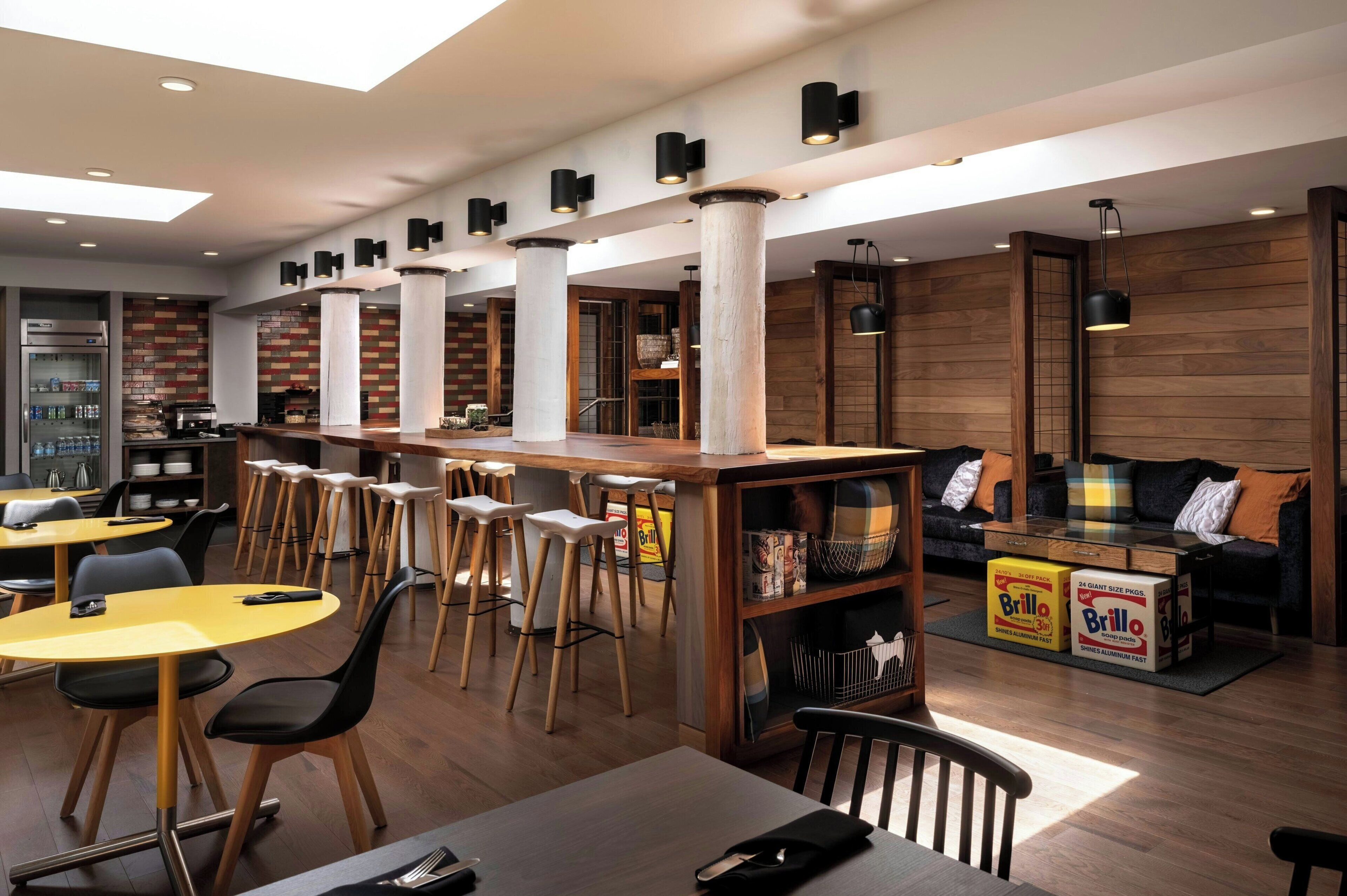 A modern restaurant with high wooden beams, multiple seating areas, and a bar counter.