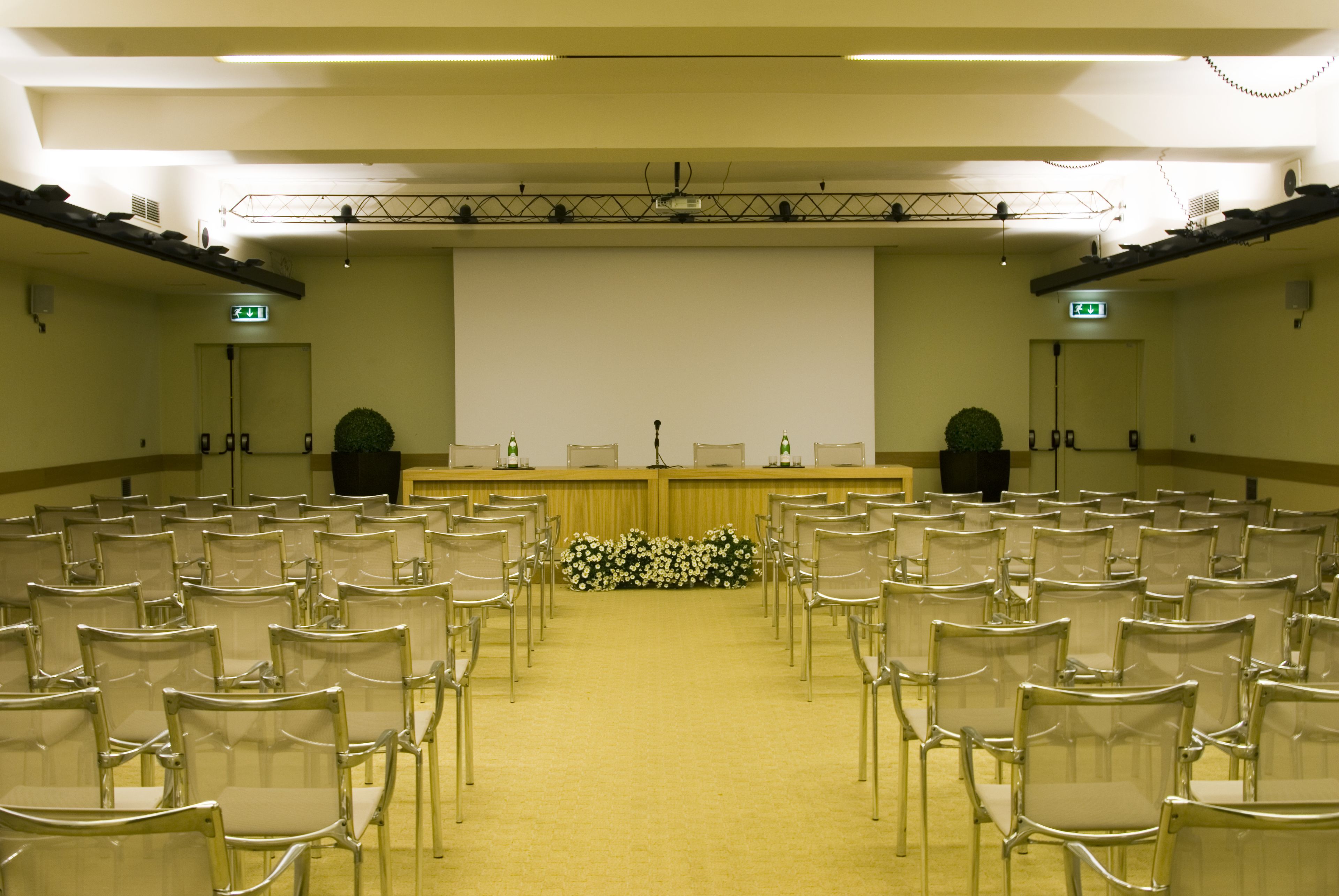 A conference room with rows of chairs, a stage with a podium, and a large screen.