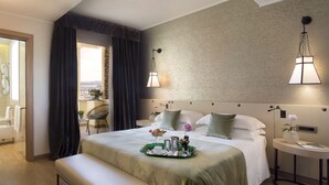 Habitación de hotel con cama, mesitas de noche, un banco, vistas de la ciudad y un balcón con silla y mesa.