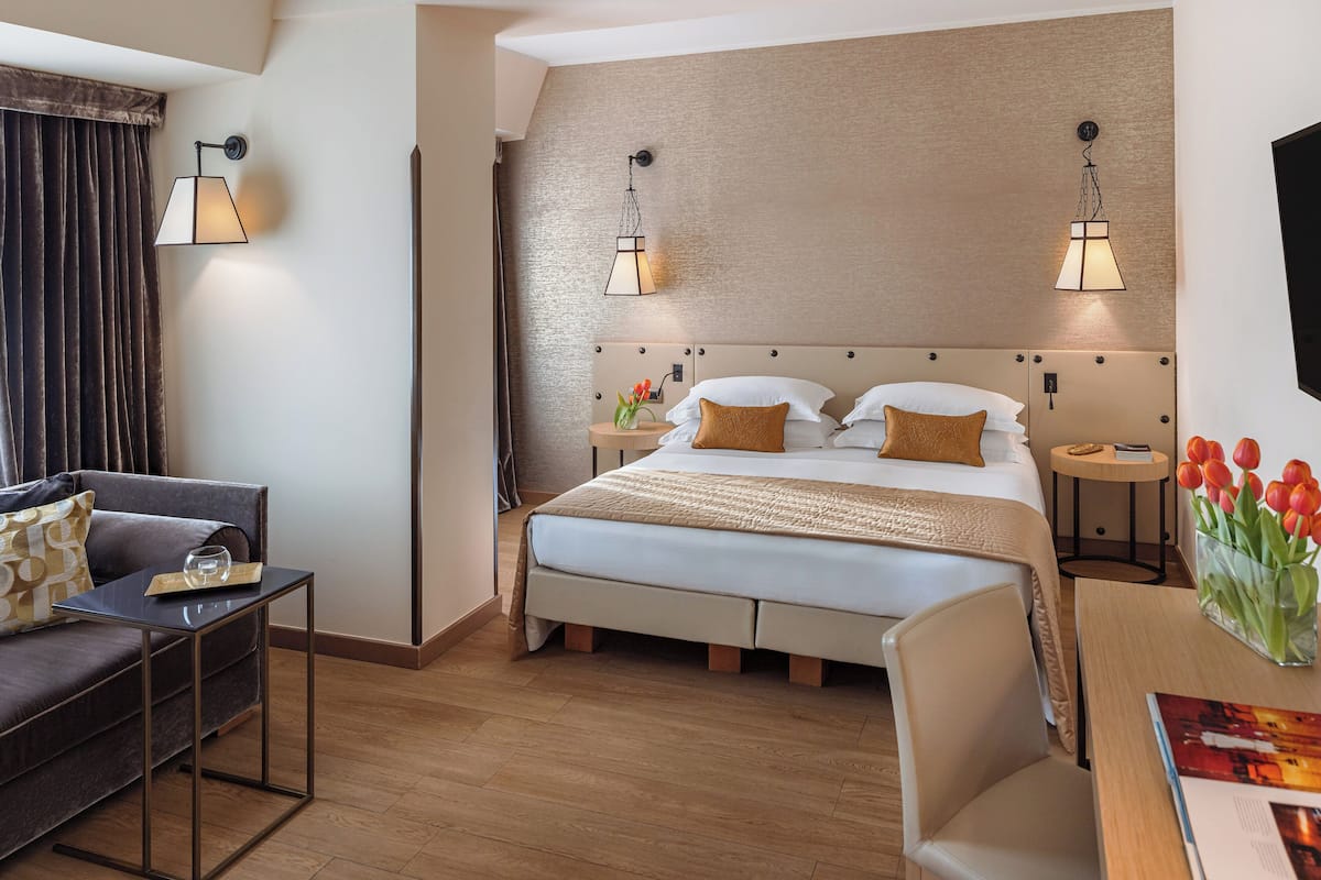 A hotel room with a bed, a sofa, a small table, and a nightstand.