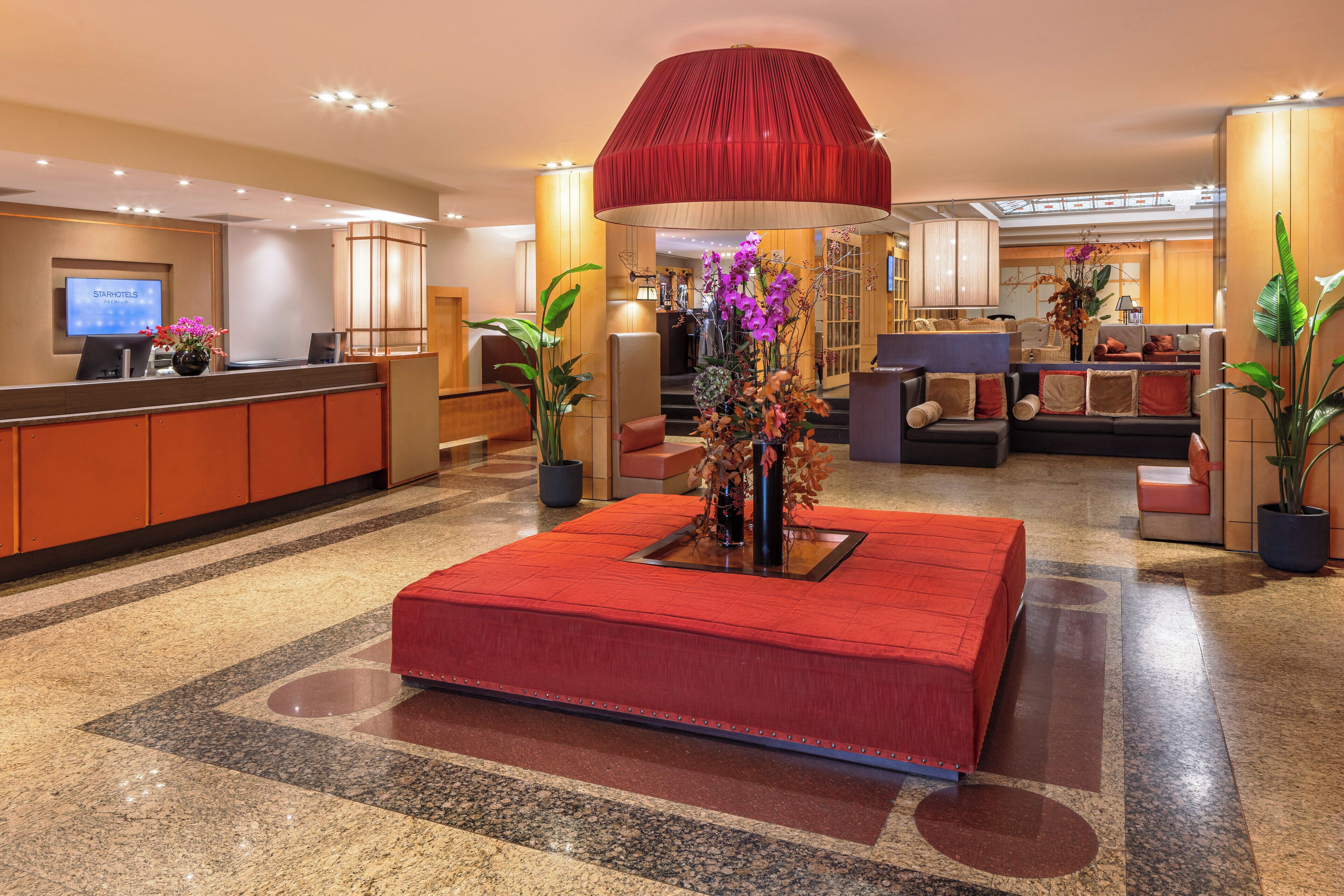Un hall de hotel con mostrador de recepción, zona de estar y una gran pieza decorativa roja.